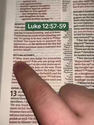 A close-up shot of an open Bible, with highlighted text and a finger pointing at a specific passage. A green rectangular text overlay displays the Bible reference 'Luke 12:57-59'. The background is filled with the text of the bible.