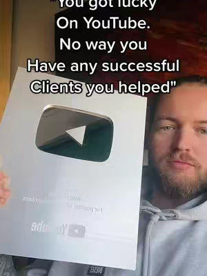 A man holds a YouTube silver play button in front of a somewhat blurry background, with the words 'You got lucky on YouTube. No way you have any successful clients you helped' overlaid on the image.