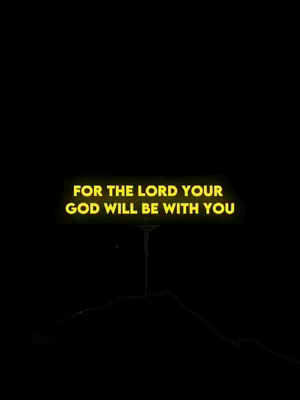 A stark, minimalist image with a black background. In the center is a slightly abstract form, possibly a stylized silhouette. Above this form, the text 'FOR THE LORD YOUR GOD WILL BE WITH YOU' is displayed in a luminous yellow font, creating a visual contrast. The overall composition is simple and emphasizes the message.