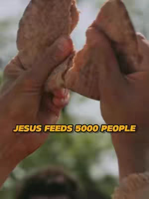 A close-up shot of two hands tearing a piece of bread, with a blurred background. Overlay text reads 'JESUS FEEDS 5000 PEOPLE'.