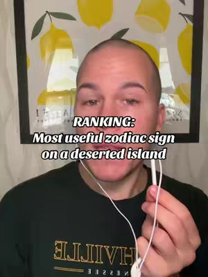 A man with a shaved head is centered in the frame in front of a print with lemons. Black text overlayed on the image says: RANKING: Most useful zodiac sign on a deserted island. The man wears a dark green shirt, and earbuds are in his ears.