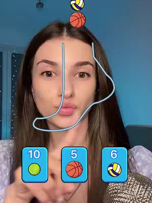 A woman with long brown hair is shown in a close-up selfie, with her face centered. There are three floating sports balls above her head. The background has a blue tint that adds depth, and the overall composition is well-lit and inviting. The woman extends her hand, pointing towards a set of number buttons laid out on the bottom.