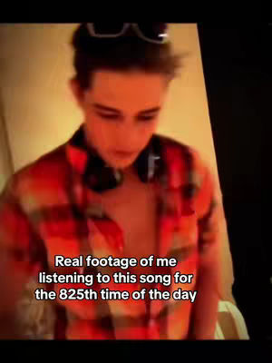 A young man in a red and orange plaid shirt with headphones around his neck gazes down, with added text overlay towards the bottom. Sunglasses rest on his head. The background seems to be a softly lit room.