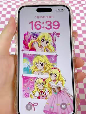 The cover image shows a smartphone displaying a customized home screen featuring illustrations from the anime series 'Aikatsu!'. The screen shows three vertically stacked images of a character with blonde hair and pink accents. The phone is held against a pink and white checkered background.