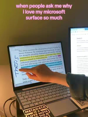 A person's hand points to the word "Thesis" on the screen of a laptop, which is open to a document with highlighted text. The laptop is on a desk, and a second monitor shows additional information. Text overlays state "when people ask me why i love my microsoft surface so much". A sticker on the laptop reads "Metadata is a love note to the future".