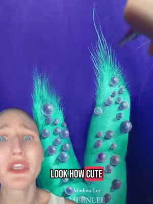 A person with a surprised facial expression is featured in the foreground. In the backdrop, a portion of an artwork with green, brush-like forms, and a blue background, is visible. Text overlays read, "LOOK HOW CUTE".