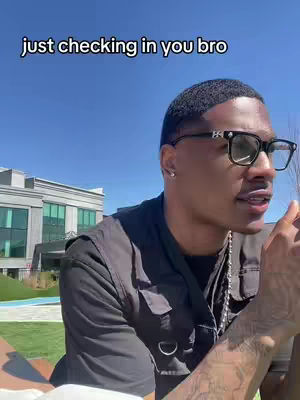 A man with glasses is standing outdoors in front of a building. Text overlayed says "just checking in you bro".