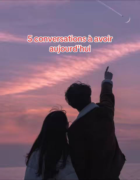A couple stands silhouetted against a vibrant sunset. The man points upward towards a crescent moon and a contrail, while the woman stands next to him. The sky is painted with hues of pink, purple, and orange.