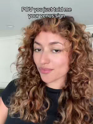 A woman with curly hair is shown in a close-up, facing slightly to the side with a subtle expression. The background is softly blurred. The image has a natural light and a warm color tone.