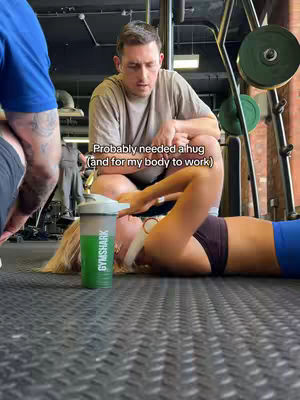 The cover image shows a gym interior with a person lying on the floor, seemingly exhausted after a workout. A man is squatting over the person looking down with concern and the other person is standing behind the man . The color palette is dark and muted due to the gym lighting.