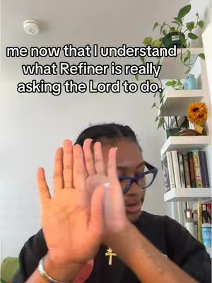 The image shows a woman with dark hair and glasses holding her hands up in front of her face with the palms facing the camera. There is text overlayed on the top of the image. The background shows a white wall, shelves, and some plants.