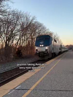 The image shows a train on a track with what appears to be a road on the side. The sky is a gradient, with colors transitioning from pink to blue, suggesting a setting or rising sun. Text is overlaid on the image.