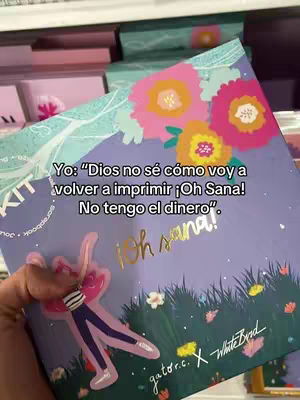 A hand holding a box with colorful flowers and text overlays. The box features a purple background with floral designs in pink, yellow, and white. Text overlaid in the image includes 'Yo: Dios no sé cómo voy a volver a imprimir ¡Oh Sana! No tengo el dinero'. A sticker of a person is in the bottom left. And more text along the bottom which includes 'gator.c. X White Bird'