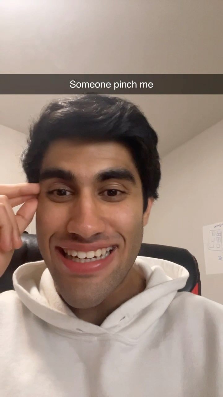 A close-up image of a smiling man with dark hair. He is wearing a white hoodie. Above him is a black bar with white text.