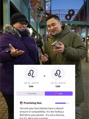 Two people are standing outside, near street lights. One is an older woman wearing a black beanie and purple coat, and a man wearing a green coat. They are both looking at a phone. On the phone screen is an astrology compatibility graphic.