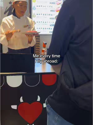 A person in a dark shirt stands in front of a food stall, with a chef holding a plate of food. The stall has a cow design with text overlaid.