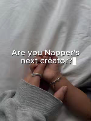 The image shows two hands clasped together, likely in a gesture of connection or support, against a neutral background. On the hands, there is a ring, and a bracelet. Text overlayed on the image asks if the viewer is Napper's next creator.