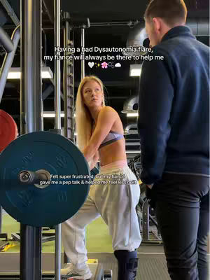 A woman with blonde hair stands in a gym setting. She's wearing a sports bra and sweatpants, leaning on a weight machine. A man, seen from the back, is standing beside her. Text overlays include a message about Dysautonomia and a countdown.