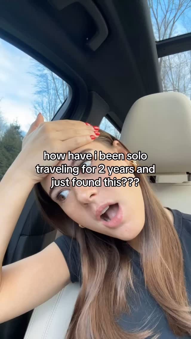 The cover image is a selfie-style shot taken from inside a car. The main subject is a woman, seen from the chest up, with a look of surprise and a hand on her forehead. She has long brown hair and is wearing a dark top. The background includes a partial view of the car's interior and a glimpse of the outside environment with trees and a blue sky visible through the open car roof. A text overlay is at the bottom.