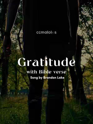A person stands with their back to the camera in a forest setting. White text overlays the image, reading 'Gratitude with Bible verse Song by Brandon Lake'. The overall color palette is muted with natural greens and browns.