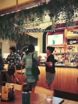 The cover image shows an interior with people standing and talking near a bar area. The scene has a warm, slightly vintage feel with subdued lighting and a neutral color palette dominated by browns and greens from the foliage. The bar area has a display with bottles and a large screen monitor.