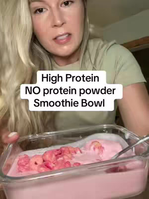 A woman with blonde hair is shown from the chest up, slightly angled from the camera view. She holds a glass dish which contains a smoothie bowl. The smoothie is pink, and topped with a pink substance. The text overlayed on the cover image reads 'High Protein, NO protein powder, Smoothie Bowl'.