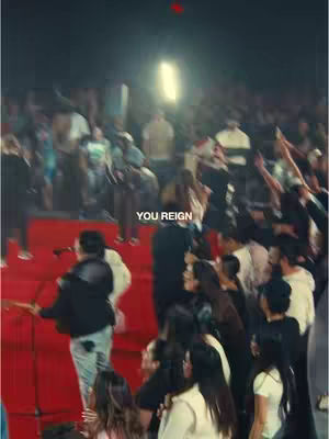 The cover image shows a crowded indoor setting, likely a worship service or concert, with a stage and a large audience. The main focus is on the performers on stage, with the crowd extending into the background. The color palette is dominated by warm tones from the stage lighting, creating a vibrant feel. The image also features overlayed text.