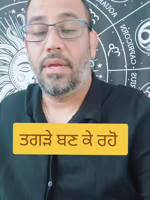 A man with glasses is the main subject of the image, seen from the chest up. He has a beard and is positioned in front of a fabric decorated with zodiac symbols. Overlaying the image is a yellow rectangle with text in a non-English language.