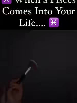 The image is a vertical shot against a dark background, featuring text at the top and a human hand holding an object in the bottom portion. The text includes the phrase 'When a Pisces Comes Into Your Life....' followed by a Pisces symbol. The hand holding an object that is black with a red mark on it in front of a completely dark background. The overall composition centers on the text that is overlaid and includes an astrology sign.