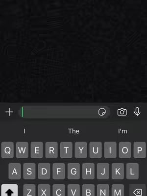 The image shows a phone screen with a dark gray background and a keyboard at the bottom. A text input bar is near the center of the screen, with a plus sign and camera icon at the edges. The keyboard shows the letters and other function keys, such as the spacebar and the return key