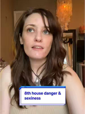 A woman with long, wavy brown hair and green eyes is in a well-lit room. She gazes upwards with a slight smile, and a text overlay box sits below her, displaying '8th house danger & sexiness'. The background is slightly blurred, with indications of a mirror and decorative lighting.