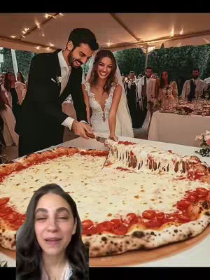 Wedding photo with a focus on the bride and groom cutting a giant pizza instead of a traditional cake. The creator is in the foreground.