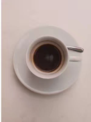 An overhead shot of a white coffee cup and saucer. The cup contains dark coffee. The spoon to stir the coffee is rested on the saucer.