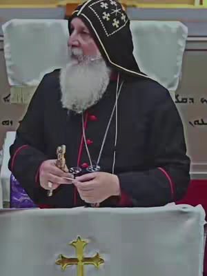 The cover image shows a man in religious attire. He has a white beard. He's wearing black robes with red trim, a black head covering with white cross patterns, and is holding a small object in his hands. A table with a gold cross is in front and a white backdrop is behind him.