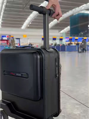 A black suitcase with a handle is being held in a hand. The background shows a busy airport terminal.