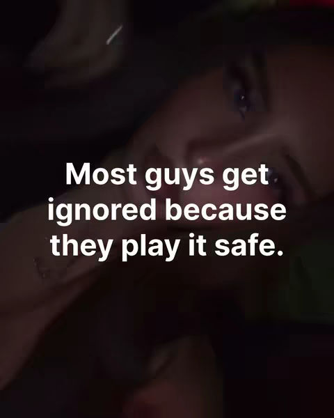 The image is a close-up, softly lit selfie of a person with dark hair and skin, seen from the chest up. The lighting is dim, creating a moody atmosphere. Overlayed on the image is white text, providing commentary. The background is a blurred dark space.