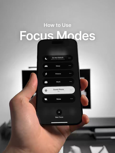 A hand holding a black iPhone displaying the settings for focus modes: do not disturb, sleep, fitness, work, dumb phone, and relax, there is text over the image that says 'how to use focus modes'. The background is a blurry gray and black.