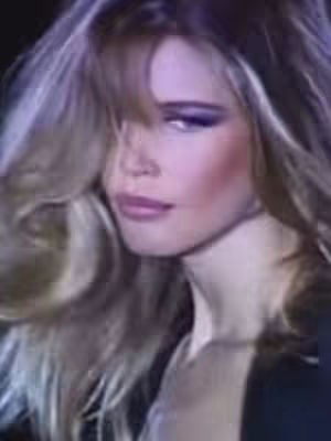 A vintage-style close-up of a woman with long, wavy blonde hair. She has full lips and is wearing makeup. The lighting suggests an indoor setting, possibly from a film or photograph.