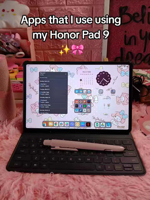 A tablet with a keyboard case is open, displaying the home screen with several app icons. A stylus is resting on the keyboard. The background is a pink, fluffy surface. The text overlay reads "Apps that I use using my Honor Pad 9". The background includes a collection of items in a pink or red setting.