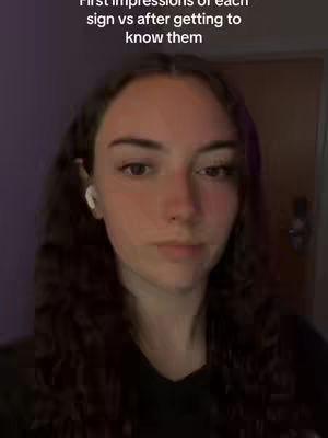 A selfie-style shot of a young woman with long, dark hair and white earphones. The image is softly lit, with a focus on the woman's face. Text overlay reads 'First impressions of each sign vs after getting to know them'.
