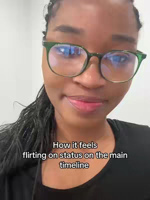 A close-up shot of a Black woman wearing glasses who is looking towards the camera and smiling slightly. The background is a blurred, neutral-colored wall. Text overlayed over the image states, "How it feels flirting on status on the main timeline."