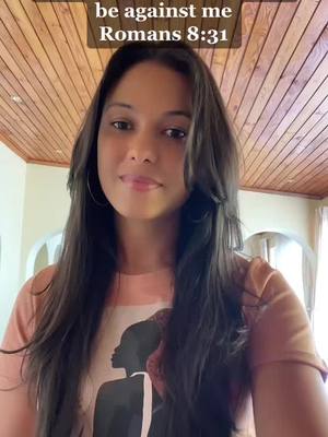 A woman with long, dark hair is centered in the frame, looking at the camera with a slight smile. She wears a light-colored top with a graphic print, and there's a wooden slat backdrop behind her. A text overlay in a dark box reads 'be against me Romans 8:31.'