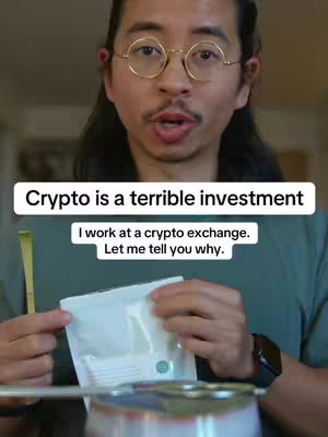 A man with glasses is centered in a selfie-style shot. He is looking directly at the camera and speaking. Above him, a white banner says "Crypto is a terrible investment", with additional white text on a banner below that says, "I work at a crypto exchange. Let me tell you why." He is pointing with his right hand to a white package with a green sticker. The background looks like a kitchen or dining setting, with blurred out details.