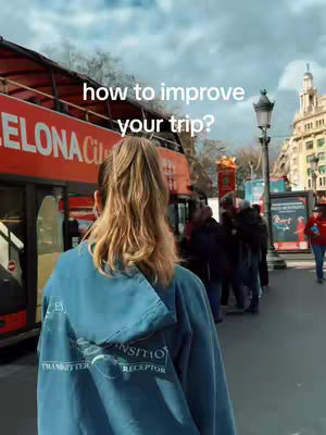 A woman with blonde hair in a ponytail, wearing a blue hoodie, stands with her back to the camera. In the background is a red double-decker bus with the text "ELONA City" visible. A street scene includes a streetlight and people in the distance.