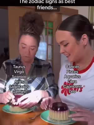 The cover image shows two women at a table, likely inside, with a focus on dessert. The woman on the left is wearing a plaid shirt and interacting with a dessert on a plate, she has text with zodiac signs around. The other woman wears a white t-shirt with a red trim, holding a dessert with the other half of signs listed on the shirt. The text appears to be part of the video's theme.