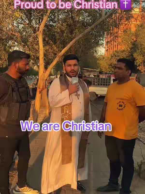 A group of three men standing outdoors. The person in the center is dressed in what appears to be religious garb and holding a phone. The other two men are standing at their side in casual clothes. Text overlays read 'Proud to be Christian' and 'We are Christian'. The background includes trees and a building.