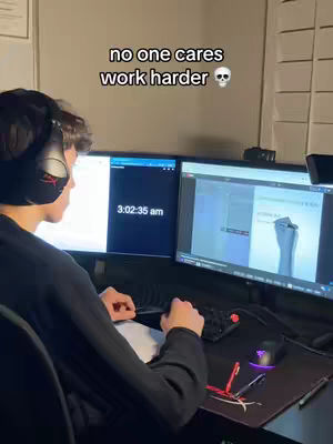 A person wearing headphones sits at a desk in front of two monitors, working on a computer setup. The lighting is dim, and the room appears to be a home office or a similar workspace. The image is composed with the person's back partially visible, creating a sense of focus on the computer screens.