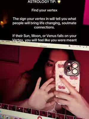 A selfie-style video filmed in a well-lit room with a red hue. The creator is holding a phone, partially obscuring their face. Text overlays and the phone's display provide context, showing the main content of the video. The overall composition seems casual with a focus on the face and the information displayed on the phone-screen.
