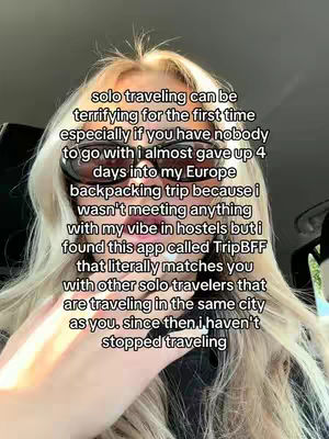 A selfie-style video cover image featuring a young woman with long blonde hair, wearing sunglasses, and looking at the camera. Text is overlaid on the image, describing her experience with a travel app. The background is blurred, typical of a selfie, with some interior details visible.