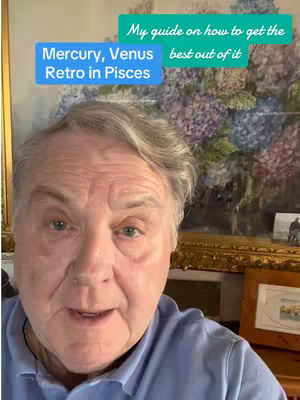 A man with gray hair and a blue shirt is centered in the frame, looking directly at viewer. Above his head are two text boxes with the words in them. Behind him is a painting with flowers.